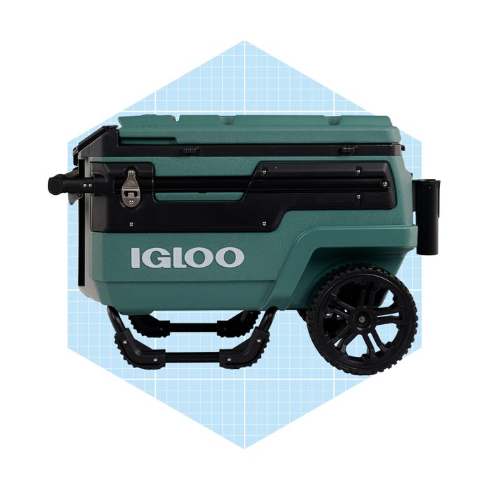 A green wheeled cooler stands upright, featuring a locking mechanism and a large handle for easy transport, set against a light blue geometric background.