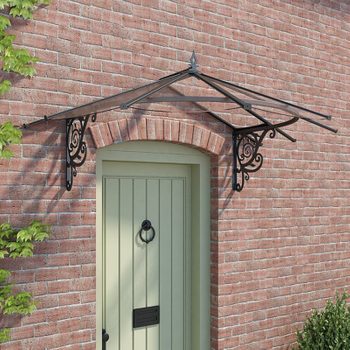 A decorative, black metal canopy protects a wooden door, set against a brick wall, surrounded by green foliage.