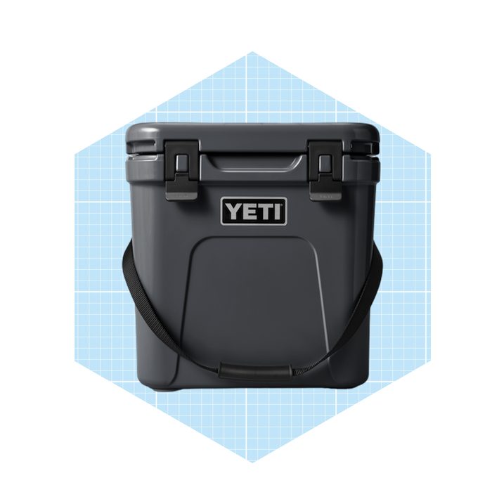 A gray cooler with a shoulder strap stands upright, branded 