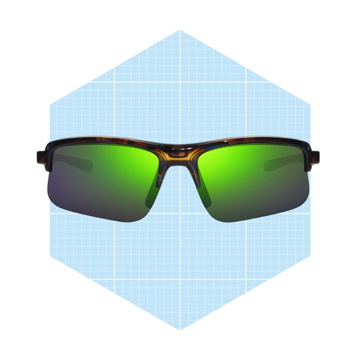 Sunglasses with green lenses are centered, resting against a light blue grid-patterned background, showcasing their design and reflecting light.