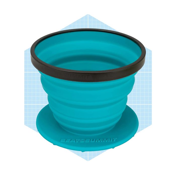 A collapsible teal cup rests on a round base, designed for portability, set against a light blue geometric background.