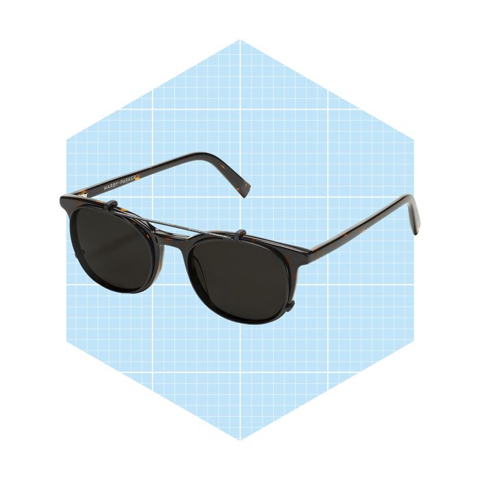 Sunglasses lie angled on a light blue hexagonal background while showcasing a dark, glossy frame and round lenses, suggesting stylish sun protection.