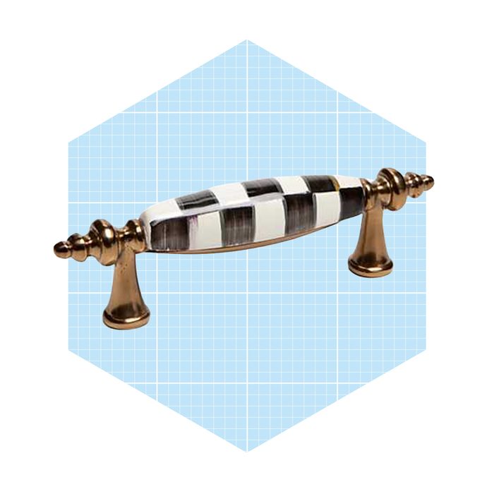 A decorative cabinet handle featuring a striped black and white design, positioned above ornate bronze bases, set against a light blue grid background.
