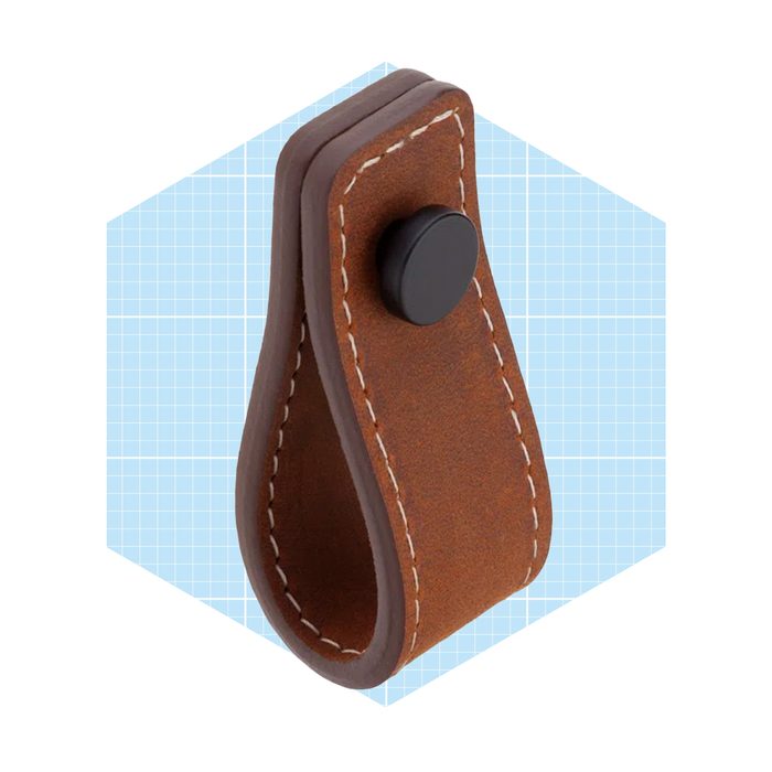 A brown leather loop with stitched edges holds a black button, suspended against a light blue grid background, suggesting a functional accessory or fastening device.