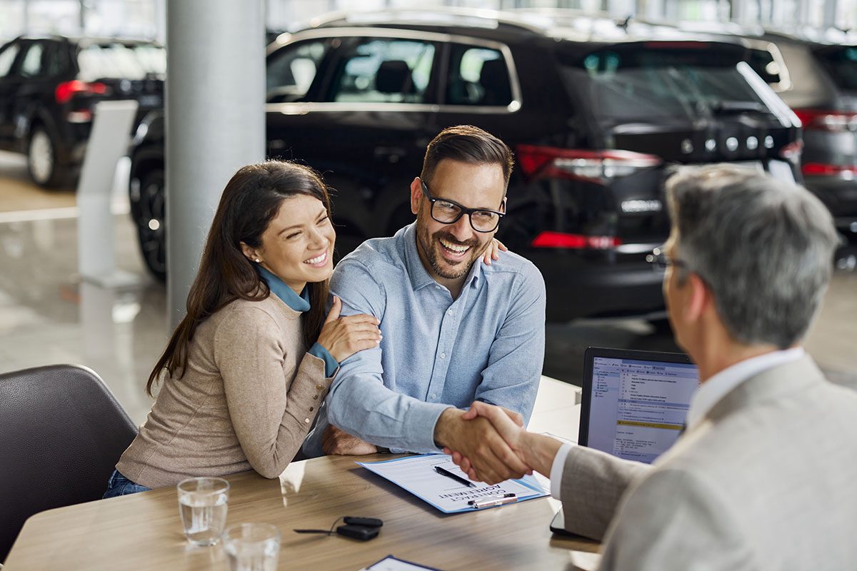 Happy couple came to an agreement with car salesperson in a showroom.